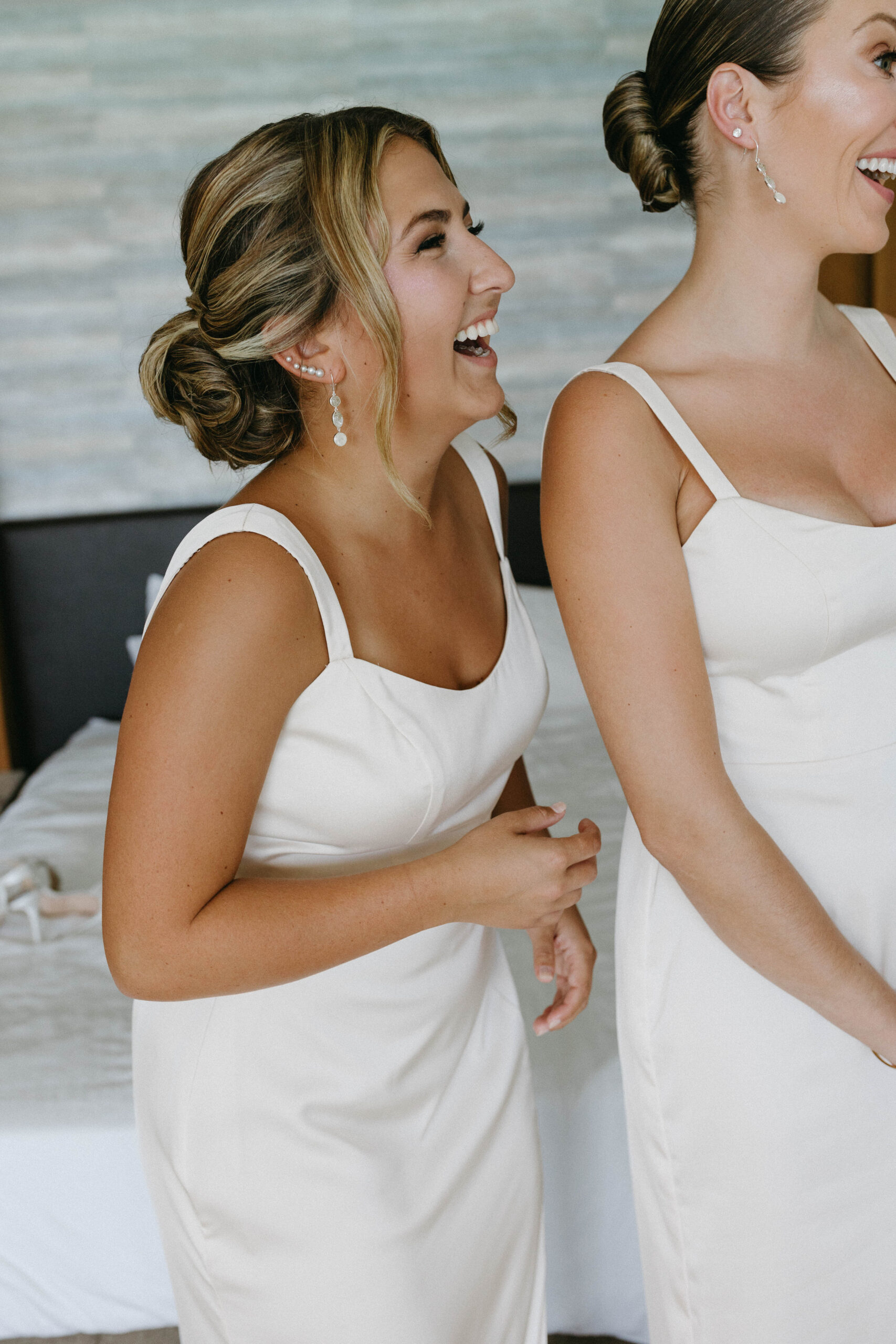 Two women who appear to be bridesmaids wearing white dresses and sterling silver jewelry smiling while looking at something off-camera.