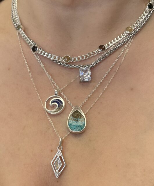 Sterling silver necklaces, including the World Traveler Necklace, layered on neck, close-up shot.
