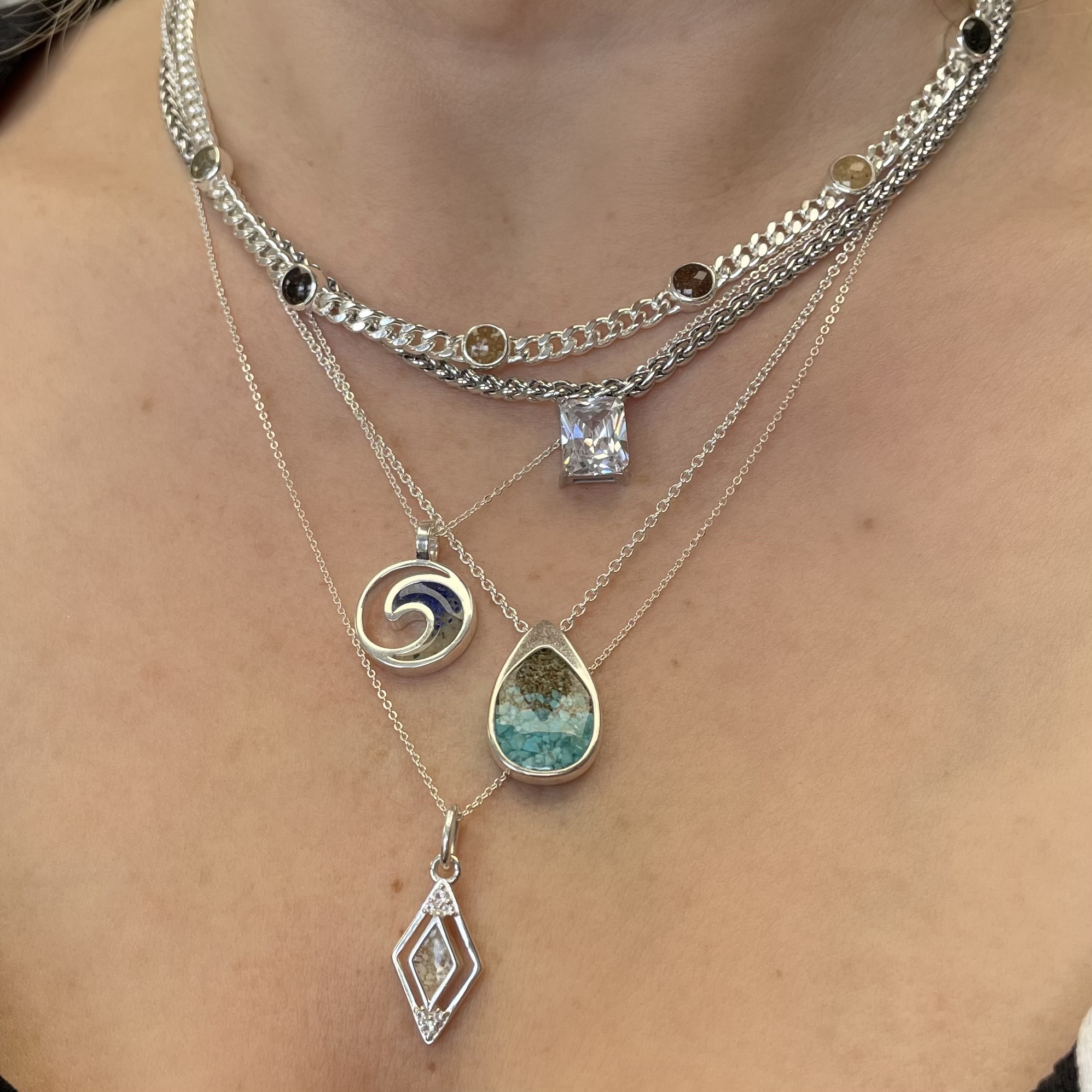 Sterling silver necklaces from Mi Tesoro and Dune Jewelry layered on neck, close-up.