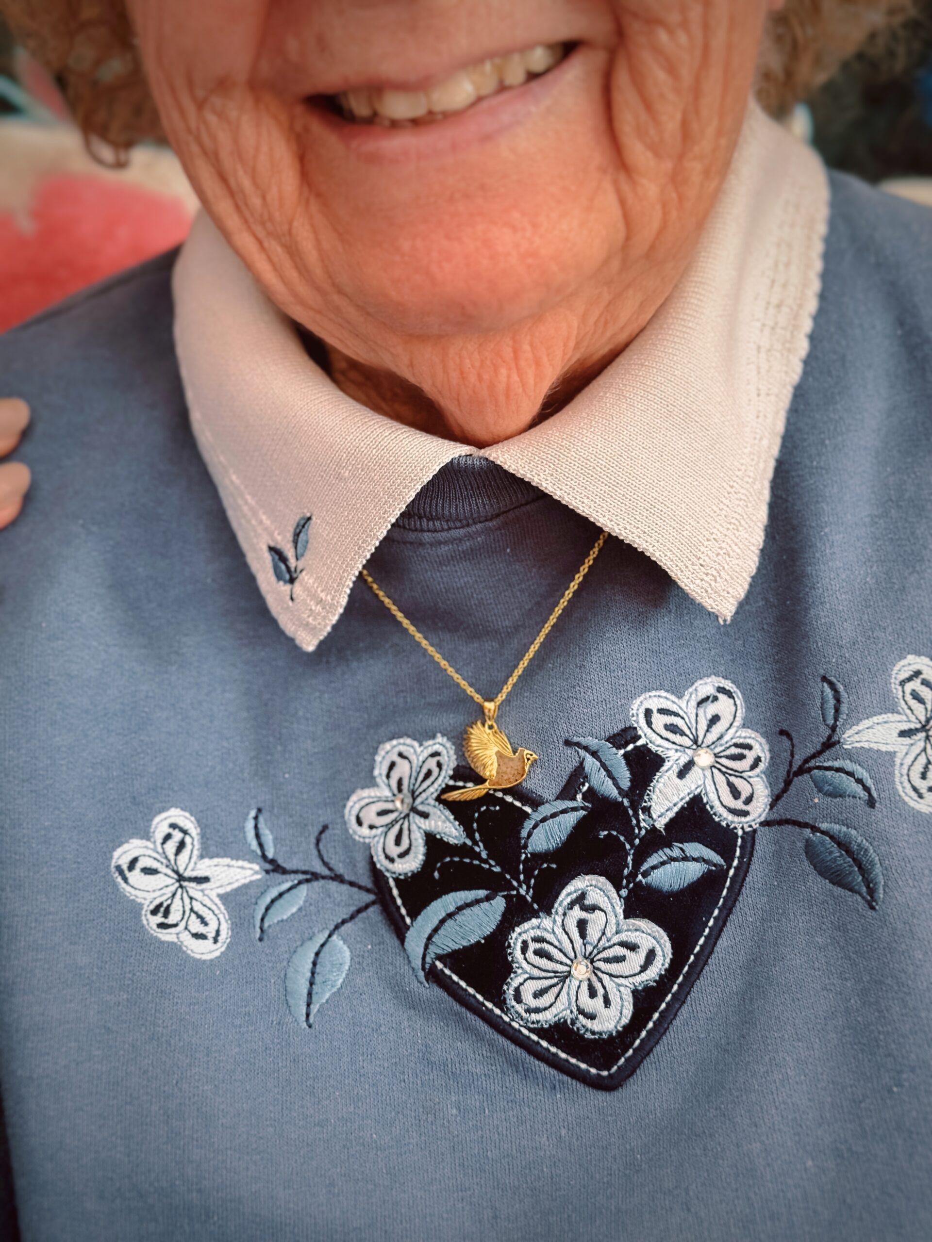 Close-up of Dune Jewelry's 14k Gold Vermeil Cardinal Necklace on the author's grandmother's neck. She is wearing a blue and white sweater.