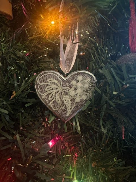 Close-up of the Dune's custom engraved heart ornament with the lace from the bride's dress inside of it, hung up on the Christmas tree.
