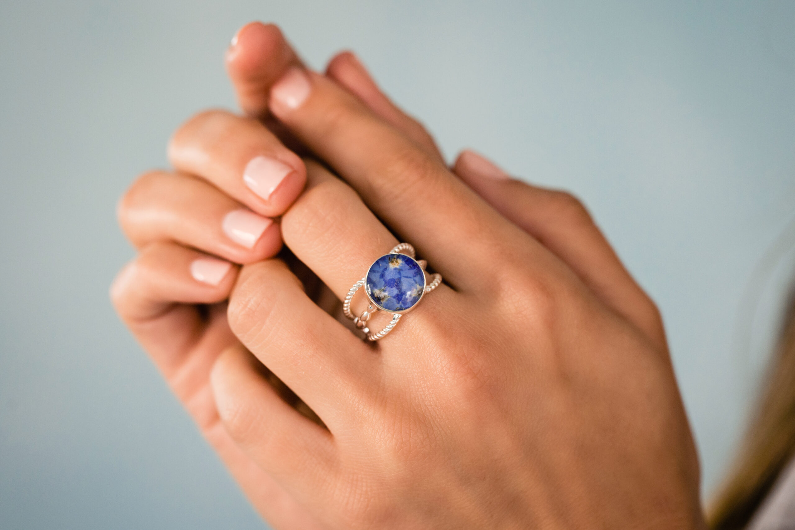 Product shot modeled on hand of the round boho ring with forget-me-not flower petals in bezel.
