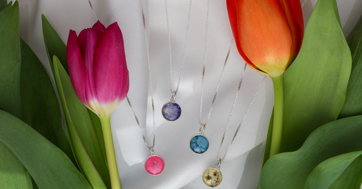 Product shot of birth month flower or spring flower jewelry surrounded by one orange and one magenta tulip and green leaves.