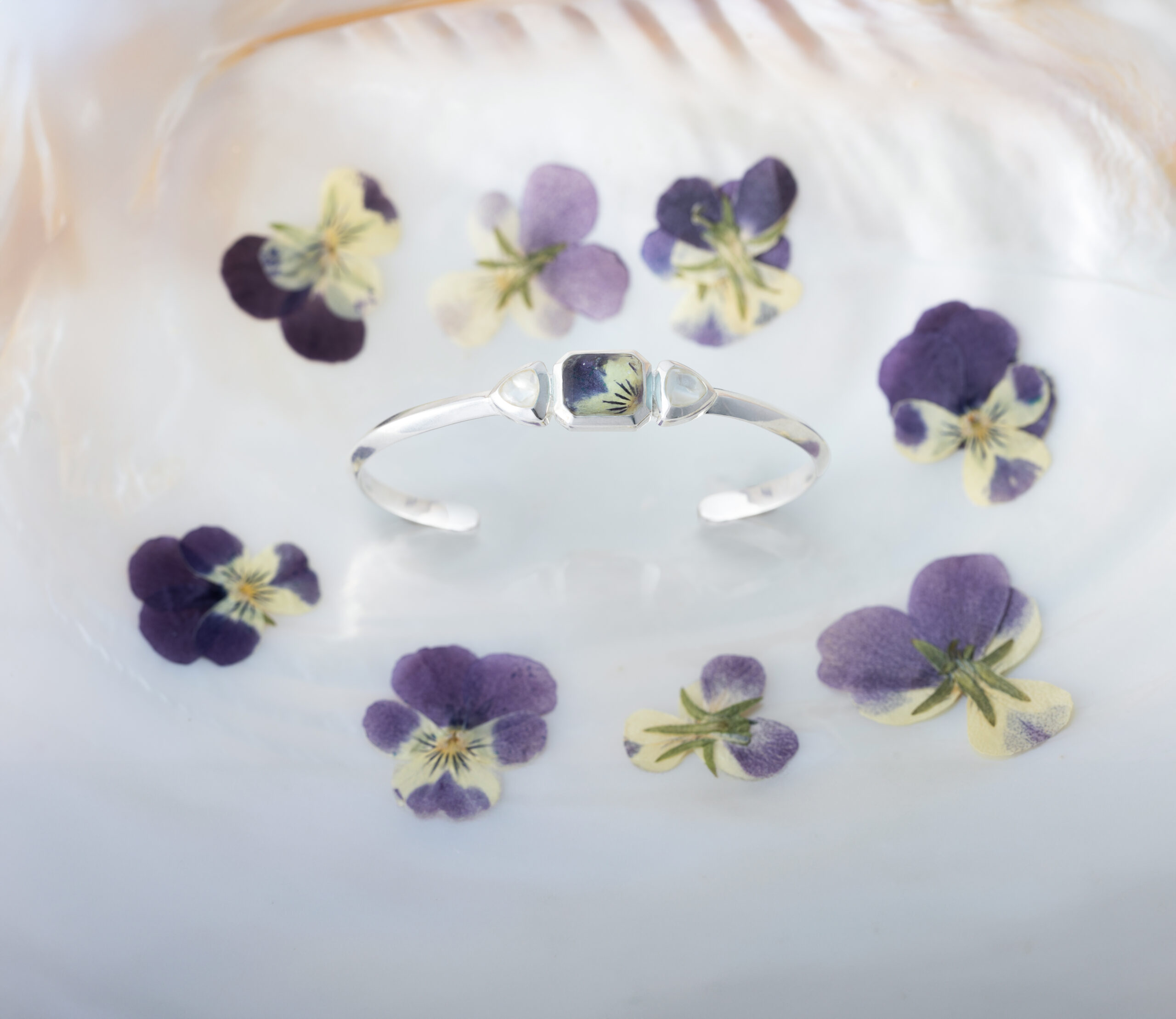 Product shot of spring flower jewelry, specifically the Serenity Cuff Bracelet with mother of pearl shell and violet flower petals