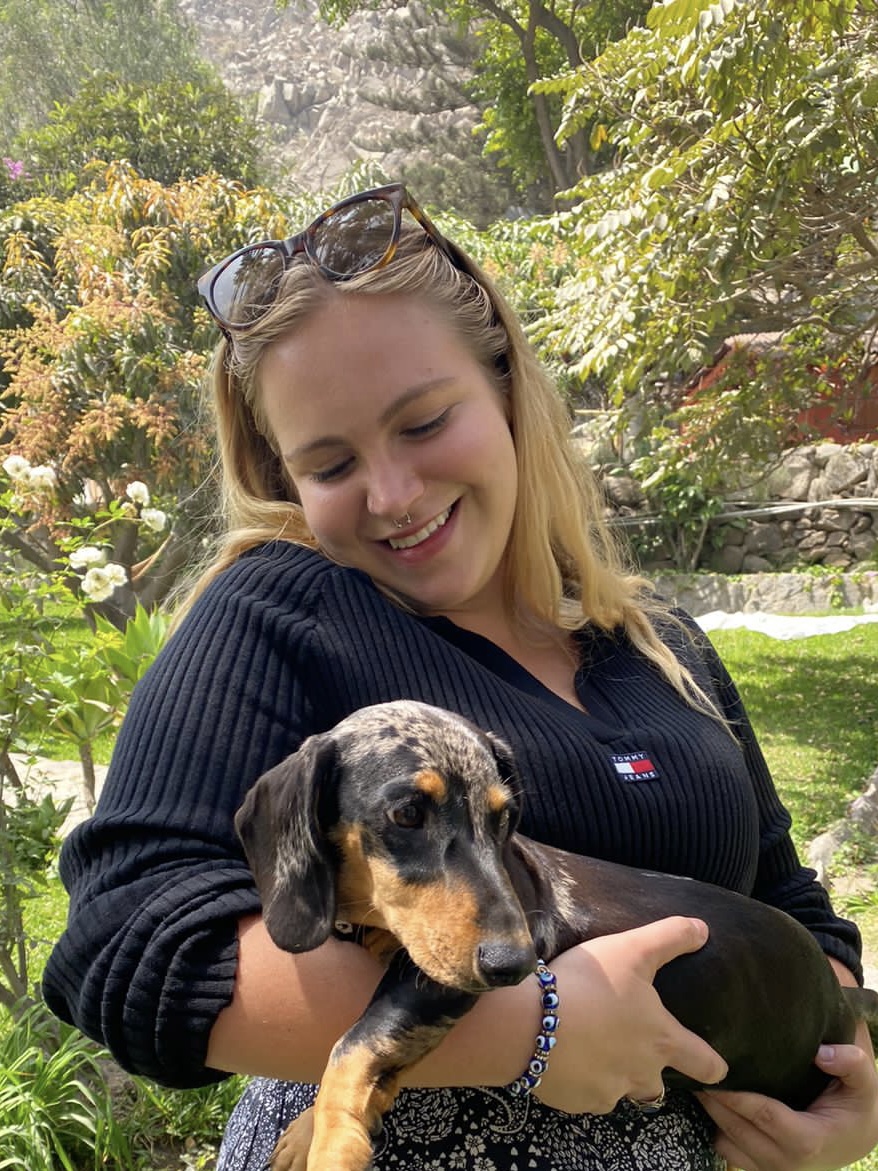Francesca, blonde, holding a black, brown, and gray dachshund puppy.