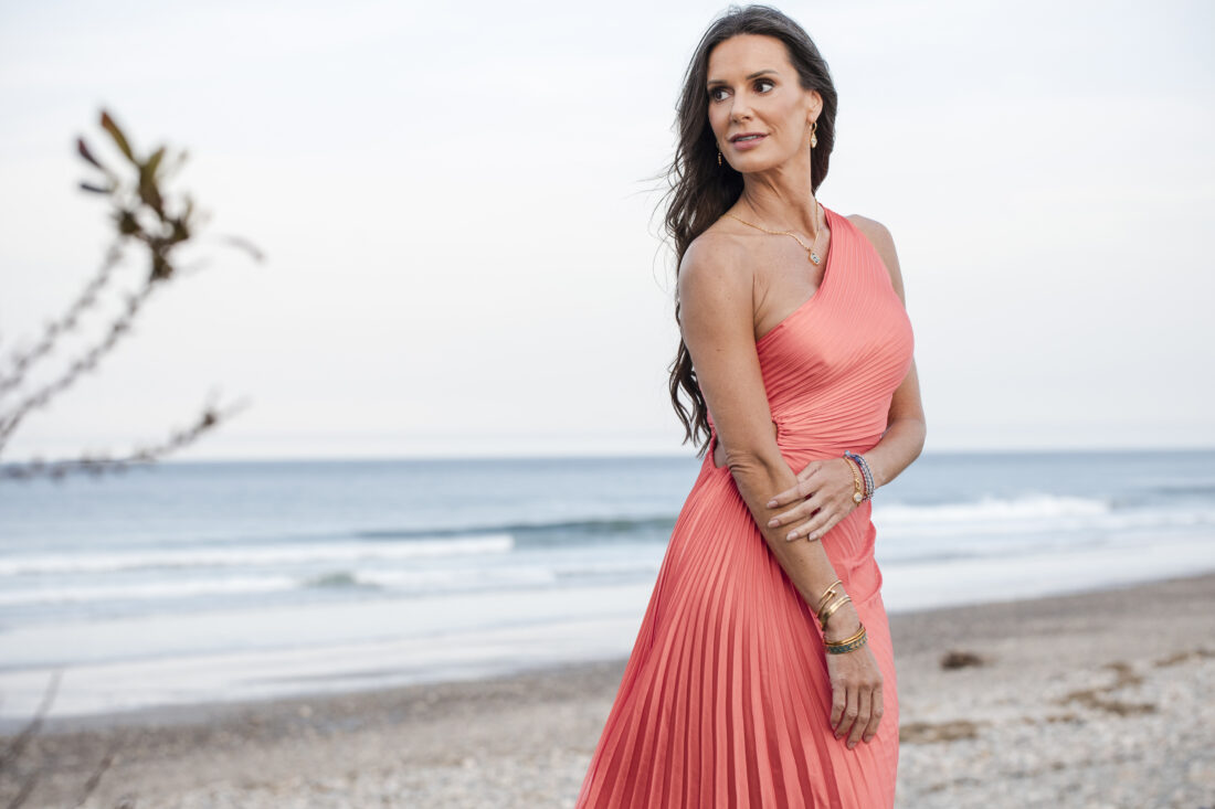 Captain Kate McCue x Dune Jewelry poses in pink dress on beach for nautical and celestial jewelry collection.