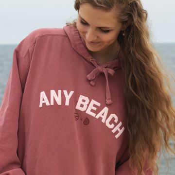 Red beach hoodie with the words any beach in white puff capital lettering.