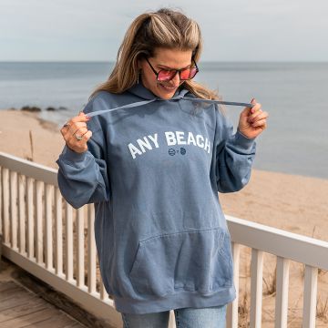 The owner of Dune, Holly, wearing a light blue beach hoodie with the words any beach in white puff capital lettering.